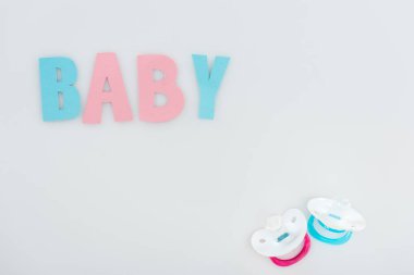 top view of pacifiers and pink and blue baby lettering isolated on white with copy space clipart