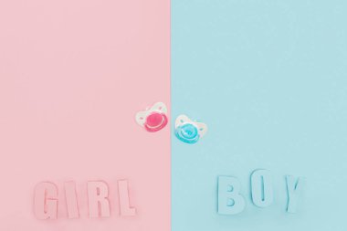 top view of pacifiers, boy, girl lettering on pink and blue background with copy space clipart