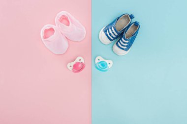 top view of pacifiers, booties, sneakers on pink and blue background with copy space clipart