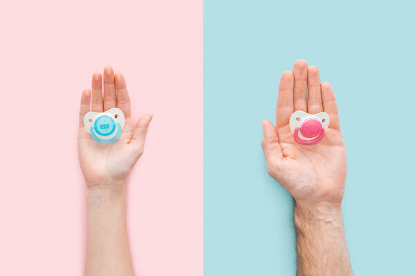 partial view of woman and man holding pacifiers on blue and pink background
