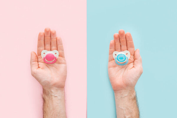 cropped view of men holding pacifiers on blue and pink background with copy space