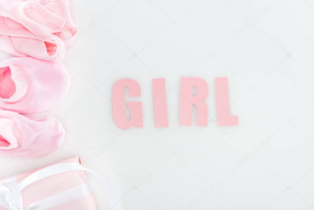 top view of pink booties, girl lettering, gift box and bonnet on white background