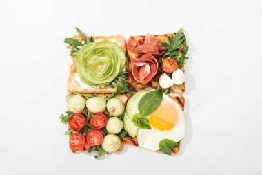 Top view of toasts with cut vegetables and prosciutto on white surface clipart