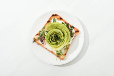 Tost dilimlenmiş avokado ve garden cress üstten görünüm plaka beyaz yüzeyi üzerinde