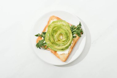 Tost dilimlenmiş avokado ve roka üstten görünüm plaka beyaz yüzeyi üzerinde