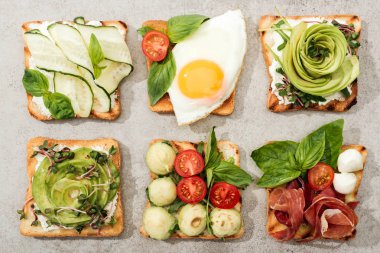 Top view of toasts with vegetables, fried egg and prosciutto on textured surface clipart