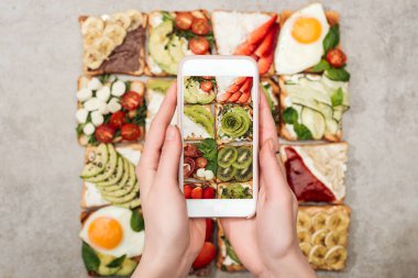 Kısmi görünümünü smartphone ve tost meyve ve sebze ile fotoğrafı çekimi tutan kadın