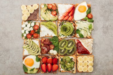 Top view of toasts with fried eggs, cut vegetables and fruits on textured surface clipart