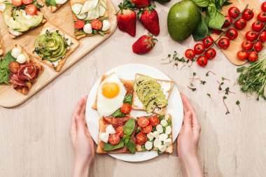 plaka sebze tost ile yeşillik ve malzemeler ile ahşap masa üzerinde tutan kadın Üstten Görünüm 