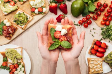 seçici odak tost domates ve prosciutto ile yeşillik ve malzemeler ile ahşap masa üzerinde tutan kadın