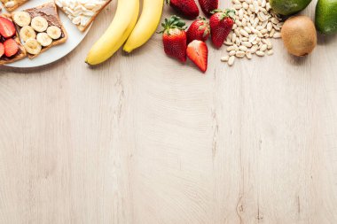 top view of bananas, strawberries, peanuts and toasts on wooden table with copy space clipart
