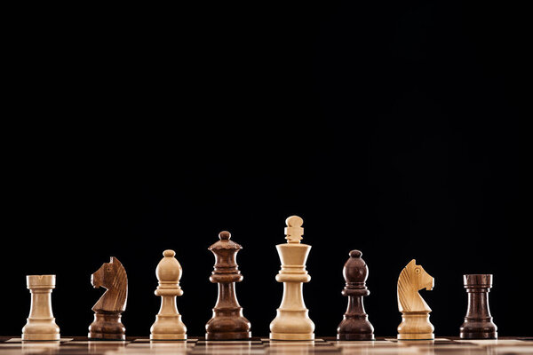 деревянная шахматная доска с коричневыми и бежевыми шахматами, изолированными на черном
 