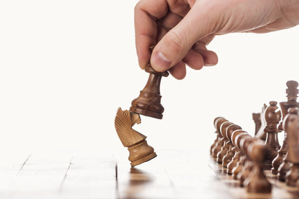 частичный вид человека, держащего пешку рядом с рыцарем на деревянной шахматной доске, изолированной на белом
