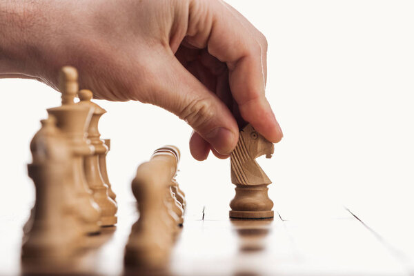 обрезанный вид человека, делающего ход с бежевым рыцарем на деревянной шахматной доске, изолированной на белом
