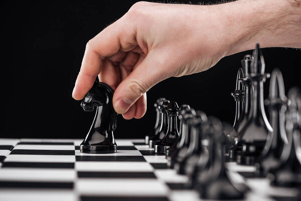 Обрезанный вид человека, делающего движение с рыцарем на шахматной доске, изолированным на черном
