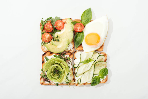 Вид сверху на тосты с жареным яйцом и нарезанными овощами на белой поверхности
