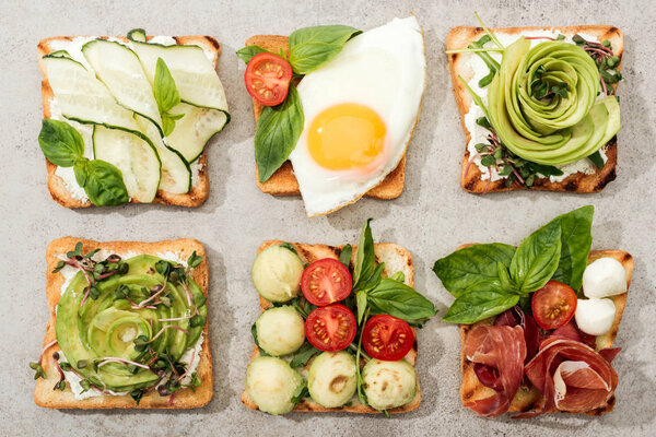 Top view of toasts with vegetables, fried egg and prosciutto on textured surface