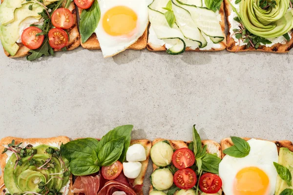Top view of toasts with vegetables, fried eggs and prosciutto on textured surface