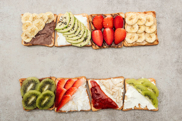 Top view of toasts with cut fruits, berries and peanuts on textured surface