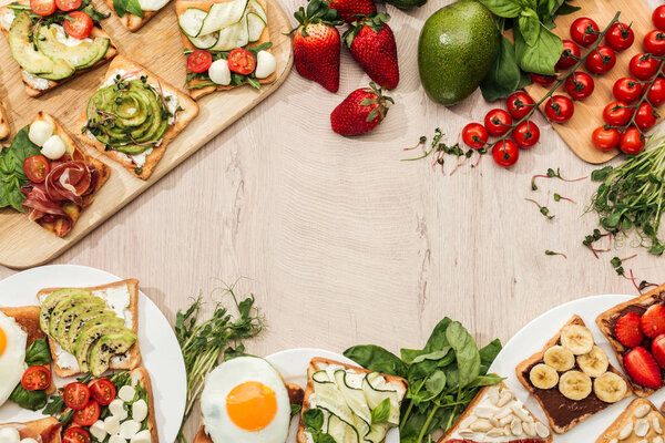 top view of toasts with vegetables, fruits and prosciutto with greenery and ingredients on wooden table