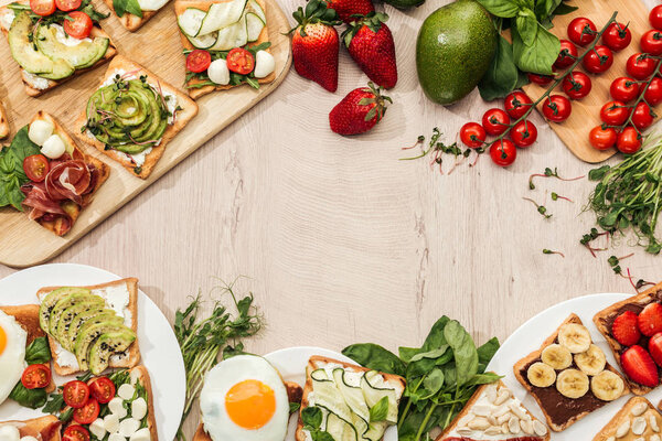 Вид сверху на тосты с овощами, фруктами и prosciutto с зеленью и ингредиентами на деревянном столе
