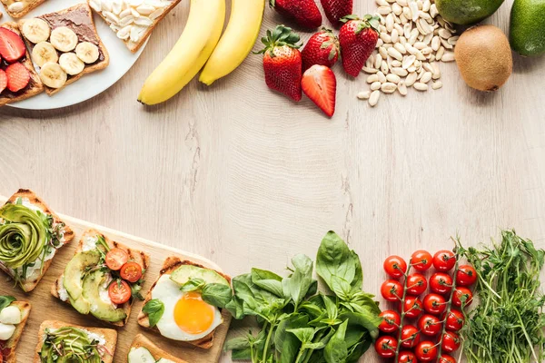 top view of ingredients on wooden table and toasts with vegetables on chopping board