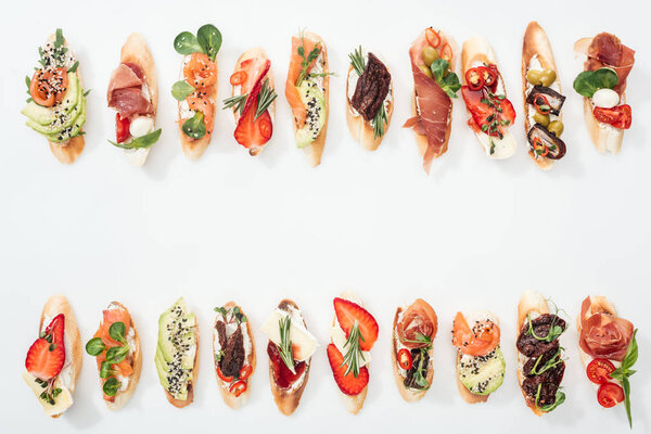 top view of traditional italian bruschetta with prosciutto, salmon, fruits, vegetables and herbs on white with copy space