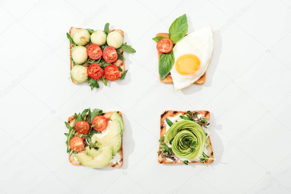 Top view of toasts with cut vegetables and prosciutto on white surface