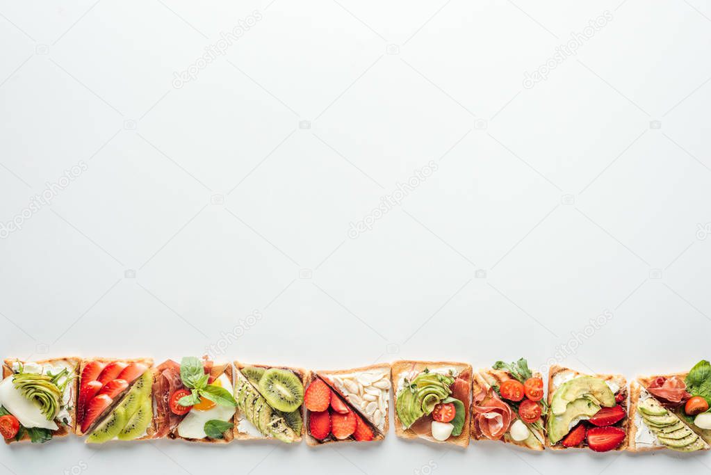 top view of row of toasts with fruits and vegetables isolated on white with copy space