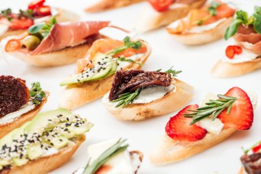 selective focus of italian bruschetta with dried tomatoes, prosciutto, avocado, strawberries and herbs on white clipart