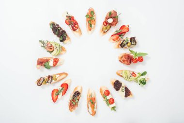 top view of round frame made of traditional italian bruschetta with salmon, prosciutto, herbs and various fruits with vegetables