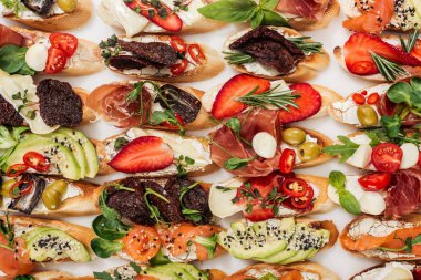 background of italian bruschetta with salmon, prosciutto, strawberries, dried tomatoes and herbs isolated on white clipart