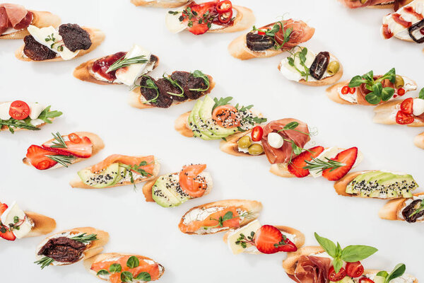 background of italian bruschetta with salmon, prosciutto, dried tomatoes, avocado, strawberries and herbs on white