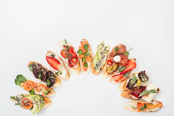 top view of delicious traditional italian bruschetta with prosciutto, salmon, fruits, vegetables and herbs on white