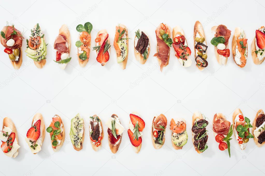 top view of delicious traditional italian bruschetta with prosciutto, salmon, fruits, vegetables and herbs on white