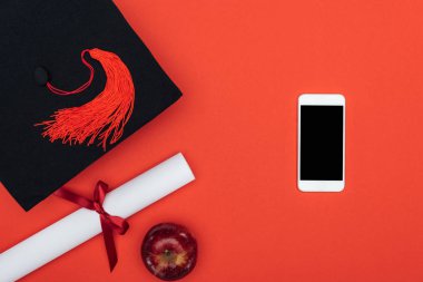 Kırmızı yüzeyi akademik kap, diploma, elma ve smartphone ile boş perde Üstten Görünüm