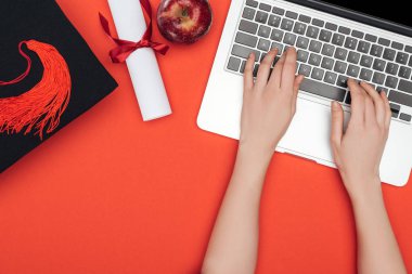 Akademik kap, diploma ve apple dizüstü kırmızı yüzeyinde kullanma ile kızın kırpılmış görünümü