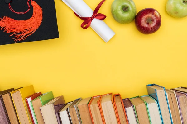 Top view of books, apples, academic cap and diploma on yellow surface