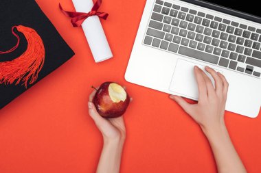 Akademik kap, diploma ve apple dizüstü kırmızı yüzeyinde kullanma ile kızın kırpılmış görünümü