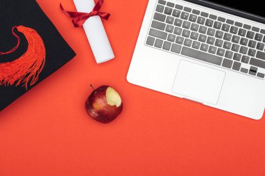 Kırmızı yüzey üzerinde laptop, diploma, akademik kap ve apple Üstten Görünüm