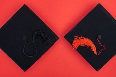 Top view of black academic caps with tassels on red surface clipart