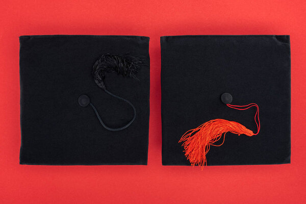 Top view of black academic caps with tassels on red surface