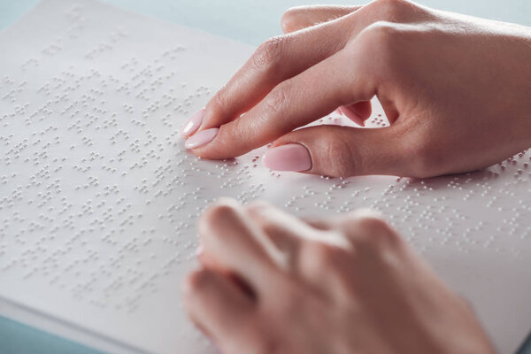cropped view of young woman reading braille text on white paper