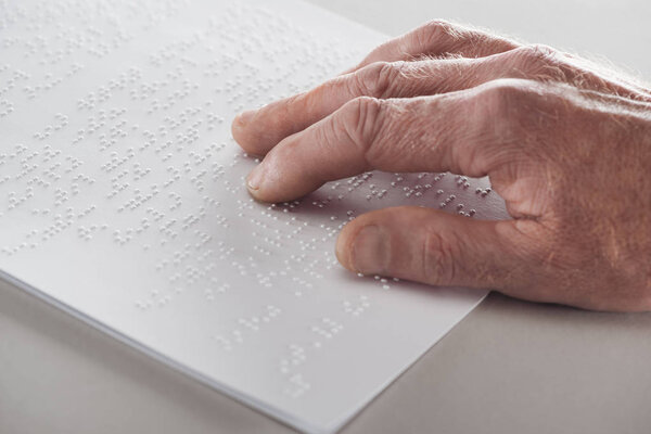 close up view of senior man reading braille text isolated on grey