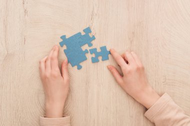 partial view of female hands with blue puzzles on wooden table clipart