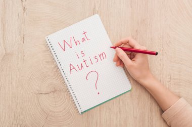 cropped view of woman writing in notebook what is autism question on wooden table clipart