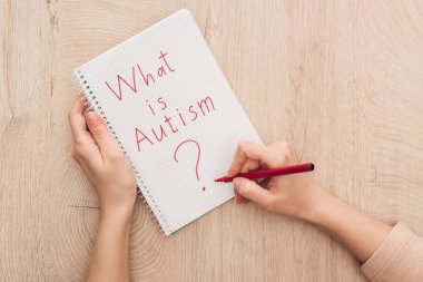 partial view of woman writing in notebook what is autism question on wooden table clipart