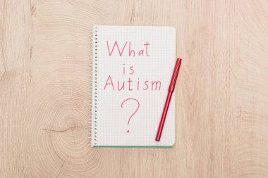 top view of red marker and what is autism question written in notebook on wooden table clipart