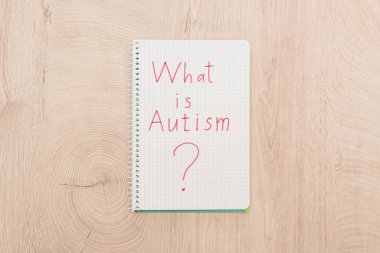 top view of red what is autism question written in notebook on wooden table clipart