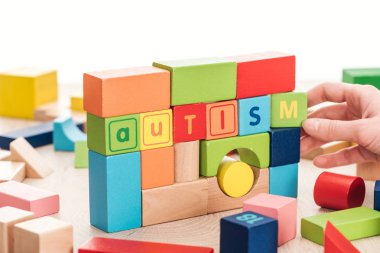 partial view of female hand near autism lettering made of colorful building blocks on wooden surface isolated on white clipart